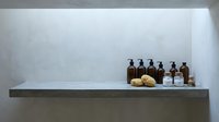Minimalist bathroom shelf with amber glass bottles and natural sponges against white wall. Modern spa wellness interior design for relaxation and self-care.