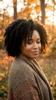 African American woman with curly hair in brown sweater enjoying peaceful autumn moment outdoors with warm golden sunlight and bokeh background.