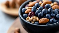 Fresh blueberries mixed with raw almonds and walnuts in black ceramic bowl, healthy breakfast ingredients and antioxidant superfood snack combination.