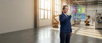 Professional businessman in dark suit using smartphone in modern industrial office space with large windows and natural lighting.