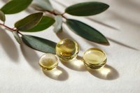 Golden vitamin E capsules with eucalyptus leaves on white fabric background for natural health and wellness skincare supplement concepts.