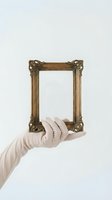 Hand wearing white glove holding ornate golden baroque picture frame against neutral background for art gallery or museum display concept.