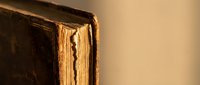 Vintage antique leather-bound book with worn golden pages and weathered brown cover against neutral background for literary and educational projects.