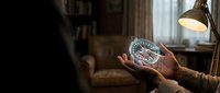 Person holding holographic brain scan display in cozy living room with warm lighting and bookshelves for medical technology and healthcare concepts.