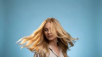 Young blonde Caucasian woman with flowing hair in motion against blue background. Dynamic portrait showcasing natural movement and energy for lifestyle content.