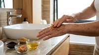 Man washing hands with natural oatmeal scrub in modern bathroom sink. Skincare routine with organic ingredients for healthy skin care and hygiene.