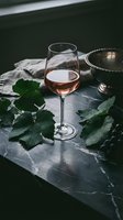 Elegant rose wine glass on dark marble surface with fresh grape leaves and vintage serving bowl creating sophisticated dining atmosphere.