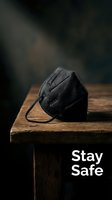 Black protective respirator mask on rustic wooden table with dramatic lighting and stay safe message for health awareness campaigns.