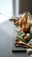 Homemade fermented vegetables in glass jars with herbs and wooden spoons on kitchen counter for healthy meal prep and food preservation.