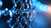 Metallic chain links in macro view against blurred blue bokeh background, creating dramatic industrial composition with depth and selective focus.