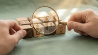 Real estate market analysis concept with magnifying glass examining wooden blocks featuring house and arrow symbols for property investment research.
