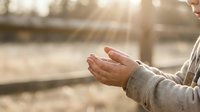 Young woman with open hands reaching toward golden sunlight in peaceful outdoor setting for meditation and spiritual wellness concepts.