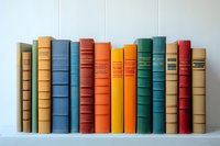 Row of vintage hardcover books in various colors standing on white shelf against light background. Collection shows classic spines in blue, orange, green and beige tones.
