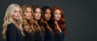 Five diverse women with long wavy hair in black outfits standing together against dark background for beauty salon marketing and hair care advertising.