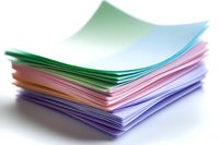 Stack of colorful paper sheets with curled edges in pastel green, pink and purple tones on white background, macro view showing layered texture and shadows.
