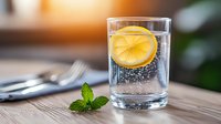 Fresh glass of sparkling water with floating lemon slice and mint leaves on wooden table, refreshing summer drink with bubbles and citrus.