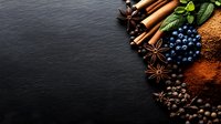 Fresh aromatic spices with cinnamon sticks, star anise, blueberries, cocoa powder and black peppercorns arranged on dark slate background with copy space.