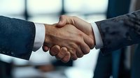 Close-up of firm business handshake between two professionals wearing suits, symbolizing trust, partnership and successful deal completion in corporate setting.
