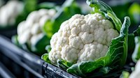 Fresh organic cauliflower head with green leaves in dark moody lighting, macro food photography showing texture and detail of white florets for cooking blogs.
