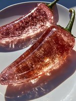 Fresh red chili peppers with water droplets on white plate creating dramatic shadows and reflections for culinary photography and spicy food concepts.