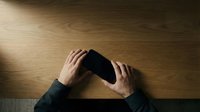 Hands holding smartphone on wooden desk surface from above, mobile device technology communication concept for business and personal use.