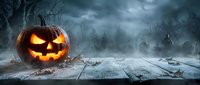 Glowing jack-o-lantern pumpkin on wooden table in spooky forest with dark stormy sky for Halloween celebration and autumn seasonal decorations.