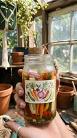 Hand holding glass jar with pickled vegetables and herb label in rustic greenhouse setting with potted plants and wooden window frames, perfect for food preservation and gardening content.