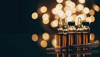 Medical vials with amber liquid in glass bottles against warm bokeh lights background for pharmaceutical research and healthcare applications.