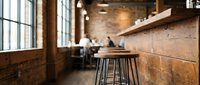 Blurred industrial loft interior with wooden bar stools, exposed brick walls, and large windows. Suitable for restaurant, cafe, and hospitality design projects.