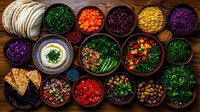 Fresh colorful ingredients in ceramic bowls with tortillas on rustic wooden table, overhead view of Mexican food preparation with vegetables, herbs and garnishes.