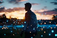 Silhouette of young Asian male against dramatic sunset sky with magical bokeh lights creating dreamy atmosphere. Artistic portrait combining natural and artificial illumination.