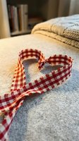 Red checkered fabric ribbon shaped into heart on cozy bed with warm lighting creating romantic atmosphere for crafts and home decor projects.