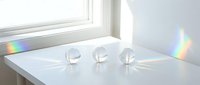 Three crystal spheres on white surface creating rainbow light refraction patterns near bright window for optical physics education and meditation decor.