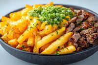 Crispy golden french fries topped with melted cheddar cheese, seasoned ground beef, and fresh chopped parsley served in black ceramic bowl on light background.