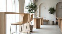 Minimalist interior space featuring wooden chairs and natural light from large windows, with potted plants and neutral tones creating a calm, contemporary design aesthetic.
