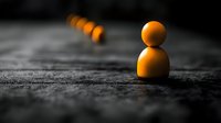 Orange wooden game pieces lined up on dark textured surface with selective focus and dramatic lighting creating leadership concept and standing out from crowd.