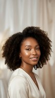 Young African American woman with natural curly hair smiling confidently in white blouse against soft neutral background for professional headshot.