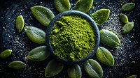Green matcha tea powder in dark ceramic bowl surrounded by fresh cardamom pods on black textured background with dramatic lighting and water drops.