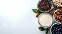 Fresh plant based milk with almonds, blueberries, chickpeas and chocolate cereals on white background. Healthy vegan protein sources and dairy alternatives.