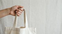 Unrecognizable person holding natural canvas tote bag against white background, suitable for eco-friendly shopping and sustainable lifestyle marketing.