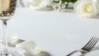 Elegant white table setting with fork, napkin and cream roses for wedding reception or fine dining restaurant event with soft romantic lighting and copy space.