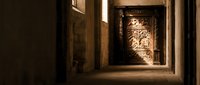Narrow alleyway with ornate wooden door illuminated by warm light, creating dramatic shadows and atmospheric ambiance for architectural and travel photography.