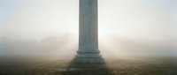 Tall stone monument column standing alone in misty fog, creating atmospheric and moody landscape scene for editorial and conceptual projects.