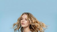 Young blonde woman with flowing wavy hair in motion against soft blue background. Natural beauty portrait with windswept hairstyle for lifestyle content.