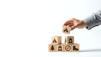 Business hand stacking wooden blocks with environmental icons showing sustainability and eco-friendly corporate responsibility concepts.