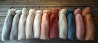 Luxurious faux fur coats in pastel and earth tones hanging on wooden rack against rustic wall background, showcasing soft textile variety and fashion display.