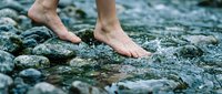 Bare feet walking on wet river stones with clear flowing water, natural outdoor adventure and wellness concept for relaxation and mindfulness activities.