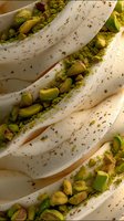 Creamy white folds of soft dessert garnished with crushed bright green pistachios creating elegant layers and textures, macro food photography with warm lighting.