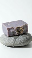 Lavender herbal soap bar with dried botanicals resting on smooth stone, isolated on white background for spa, wellness, and cosmetic product design use.