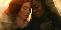Intimate portrait of two women, redhead and African American, in warm golden light with closed eyes touching foreheads, expressing unity and tender connection.